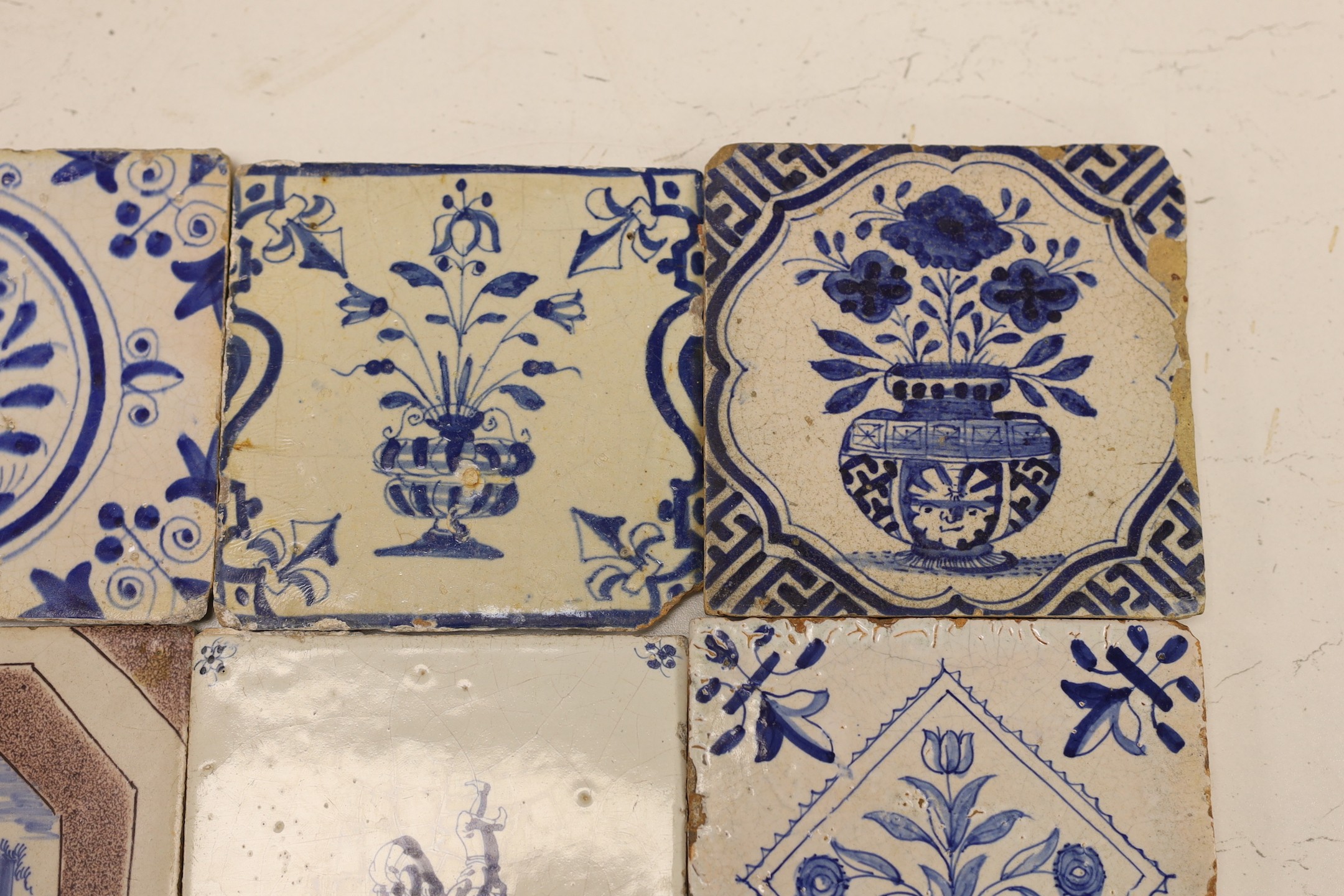 Four mid 17th century Delft blue and white ‘urn of flowers’ tiles, and an 18th century Delft ‘acrobats’ tile and blue and manganese ‘landscape’ tile (6)